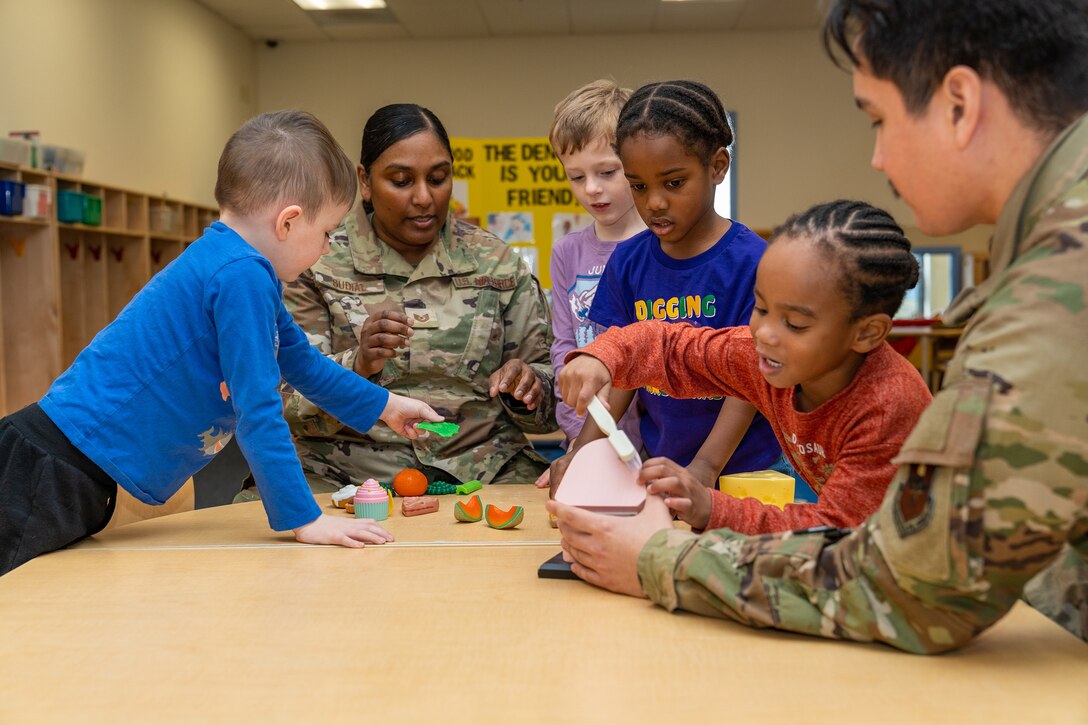 Two airmen show four children how to brush their teeth during an oral health demonstration.