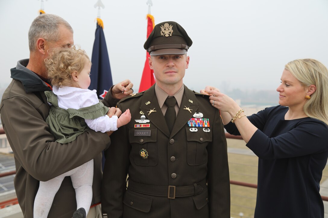 A soldier is pinned by two family members, one holding a child, during a promotion ceremony.
