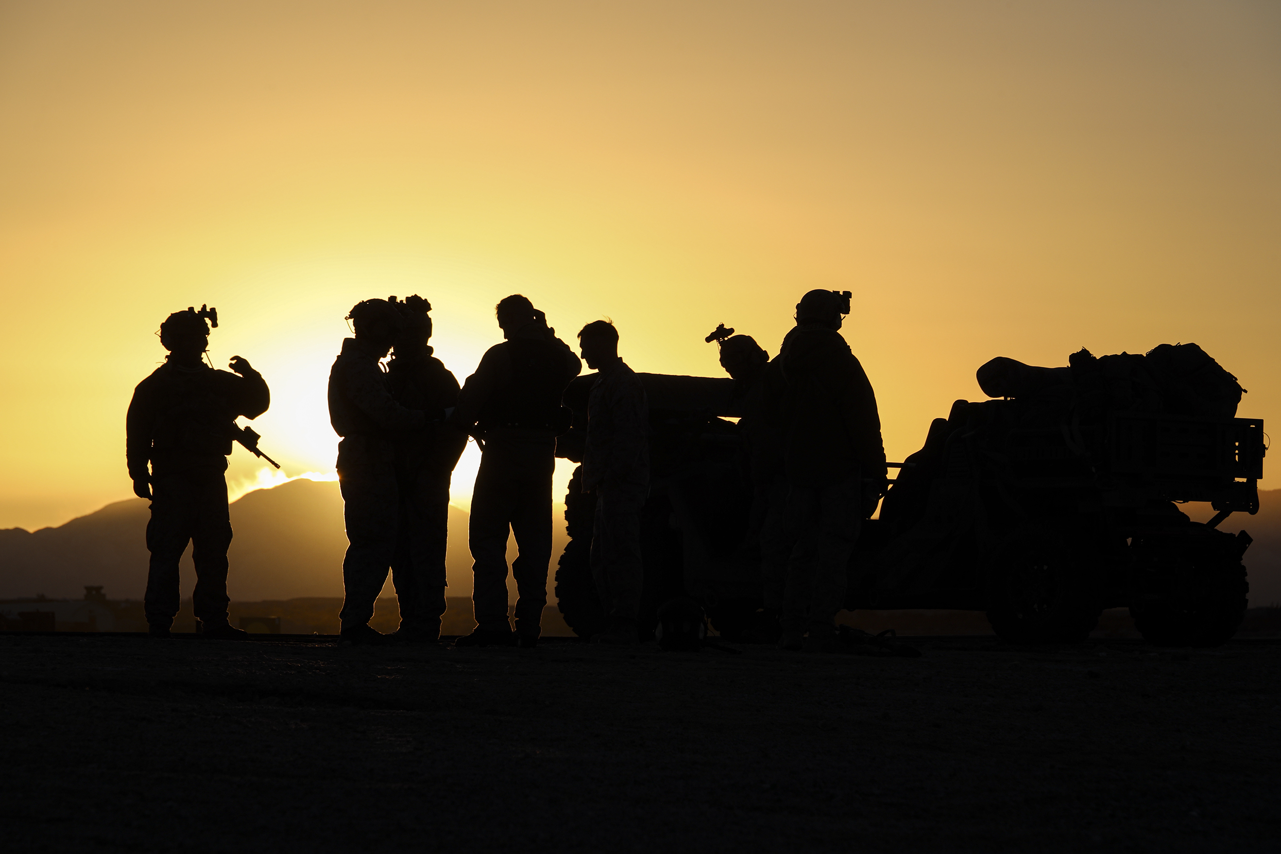 People in military uniforms are shown in silhouette standing near a tactical vehicle.