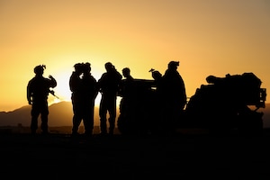 People in military uniforms are shown in silhouette standing near a tactical vehicle.