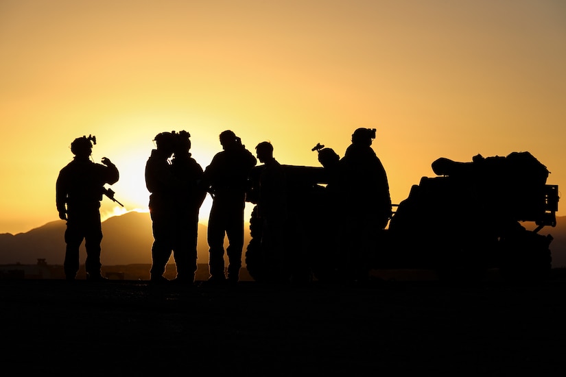 A group of Marines are shown in silhouette standing near a tactical vehicle.