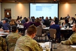 Conference room of Family members seated looking at a presentation being given on a large screen.