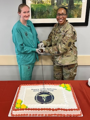 Two nurses cutting a Birthday cake with a sabre.