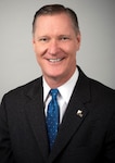 A light skinned man with brown hair in a dark business suit.