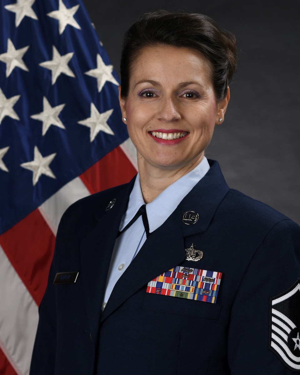 Official photo of MSgt Joanne Griffin.  MSgt Griffin serves as Regional Band Vocalist and First Sergeant with the United States Air Force Band of the Pacific-Asia at Yokota AB, Japan.  MSgt Griffin is wearing blue service dress uniform in front of the red white and blue American flag.