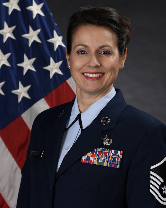 Official photo of MSgt Joanne Griffin.  MSgt Griffin serves as Regional Band Vocalist and First Sergeant with the United States Air Force Band of the Pacific-Asia at Yokota AB, Japan.  MSgt Griffin is wearing blue service dress uniform in front of the red white and blue American flag.