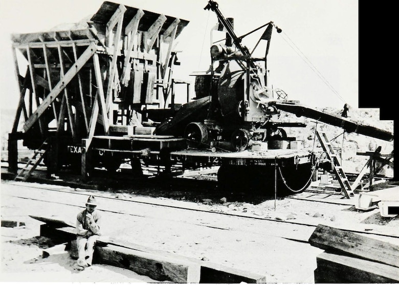 A small concrete mixer moved along railroad tracks to pour concrete into the base for the east end of the Galveston Seawall extension, circa 1920.