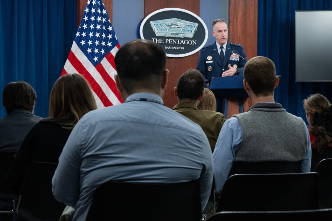 A man in a military uniform stands at a lectern.