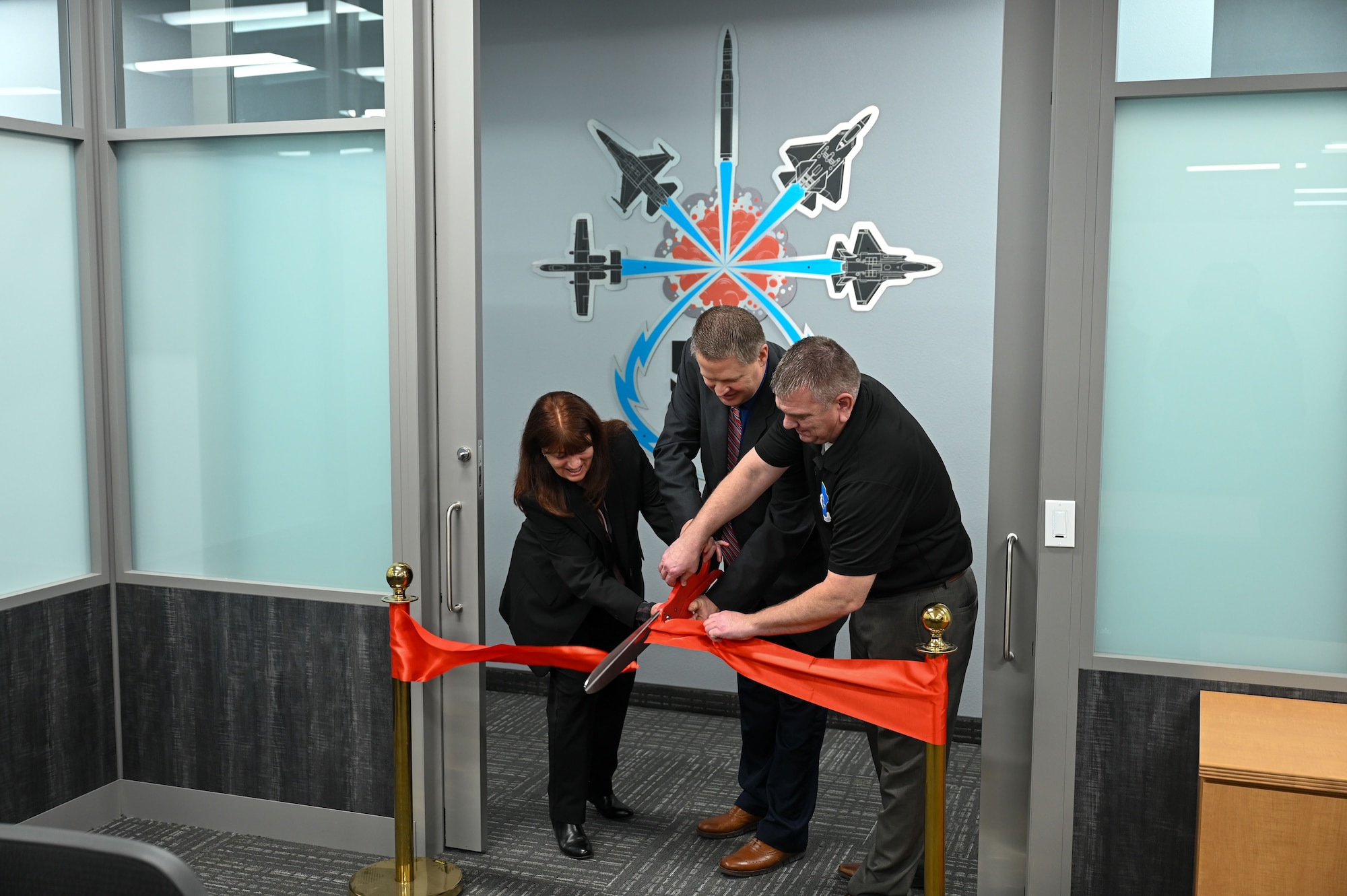 Three civilian members are cutting the ribbon at a new office.