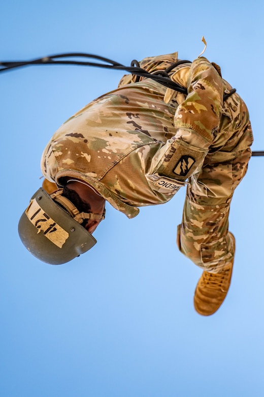 A soldier rappels upside down.