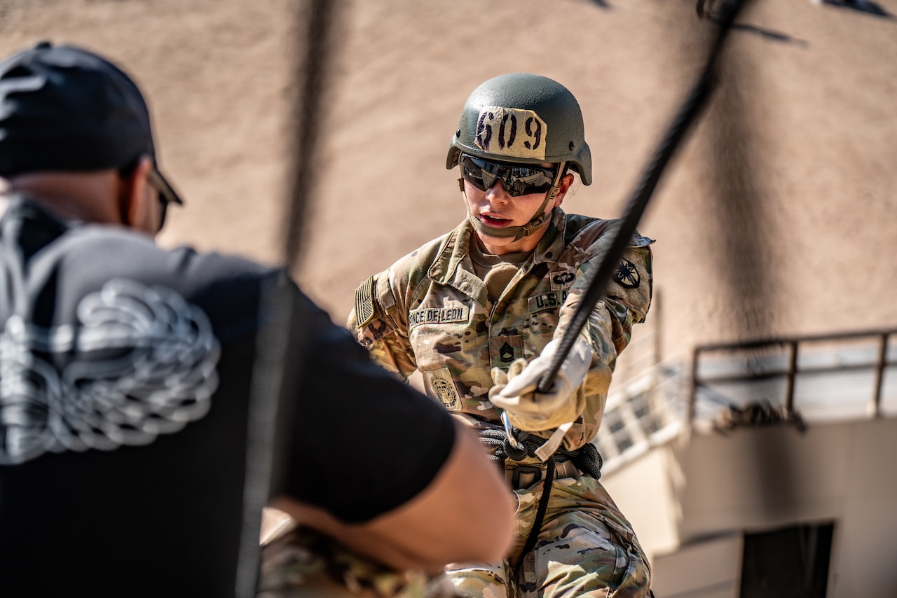 A soldier helps a fellow soldier rappel down a tower.