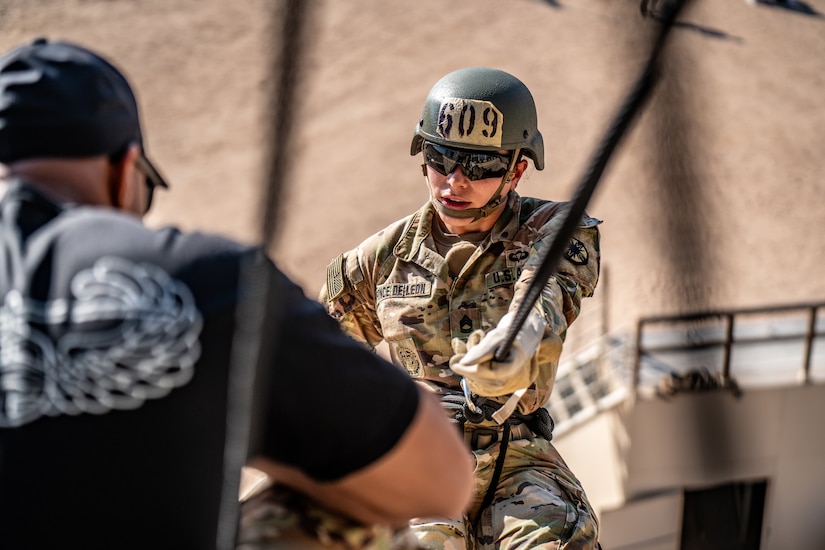 A soldier helps a fellow soldier rappel down a tower.