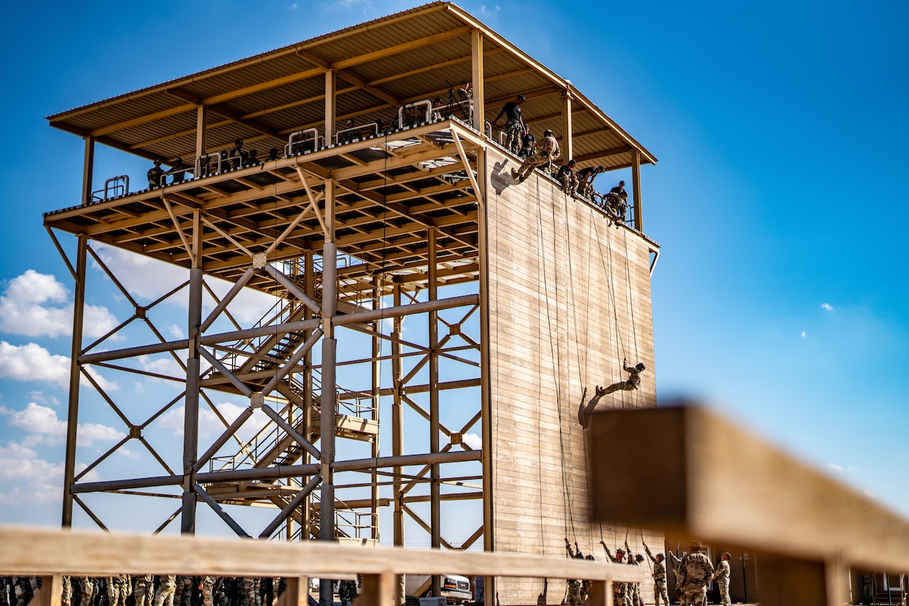 A soldier rappels from a tower as seen from the side.