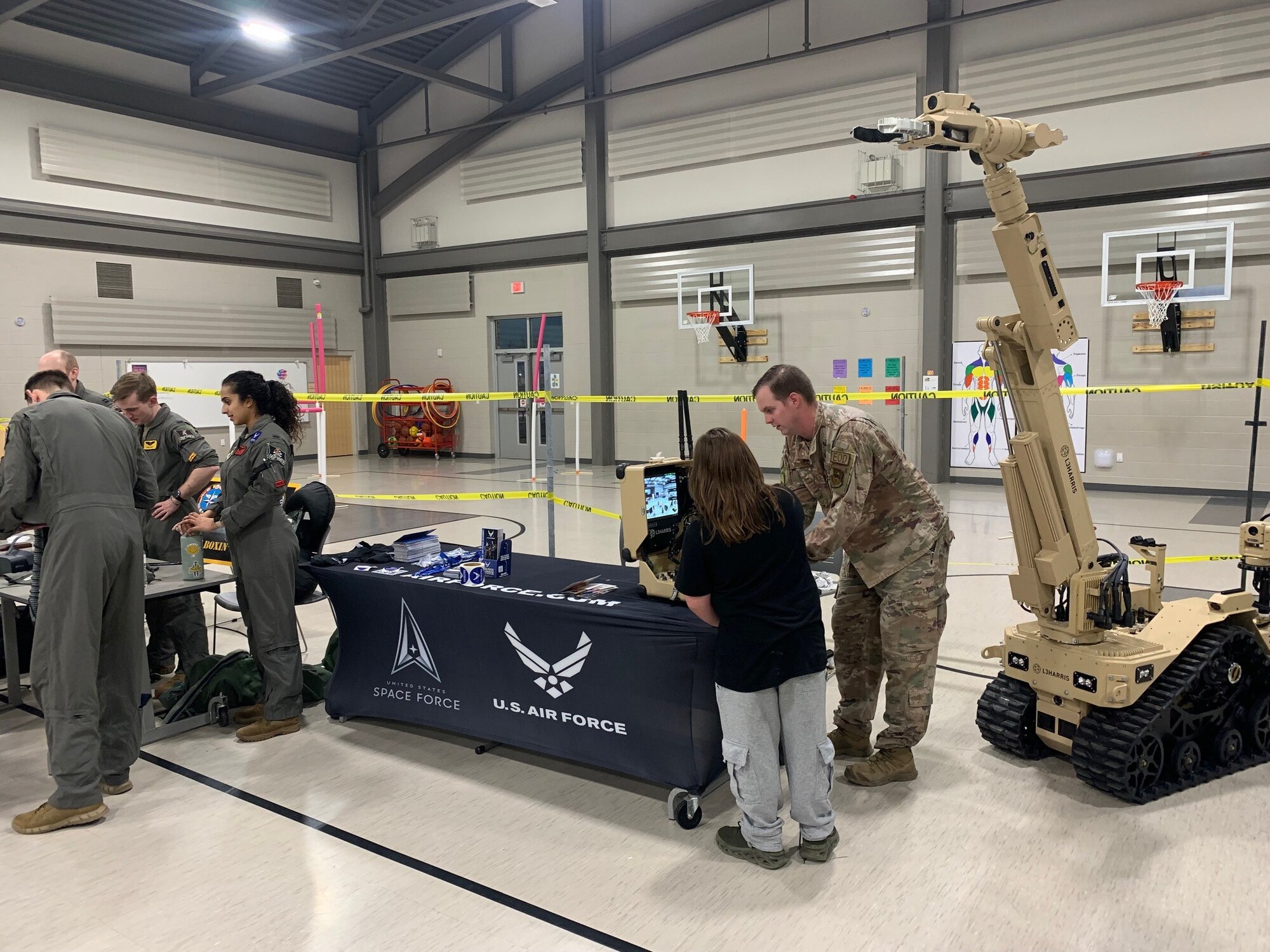 Airmen stand at tables talking with children. There is a robot in the background.