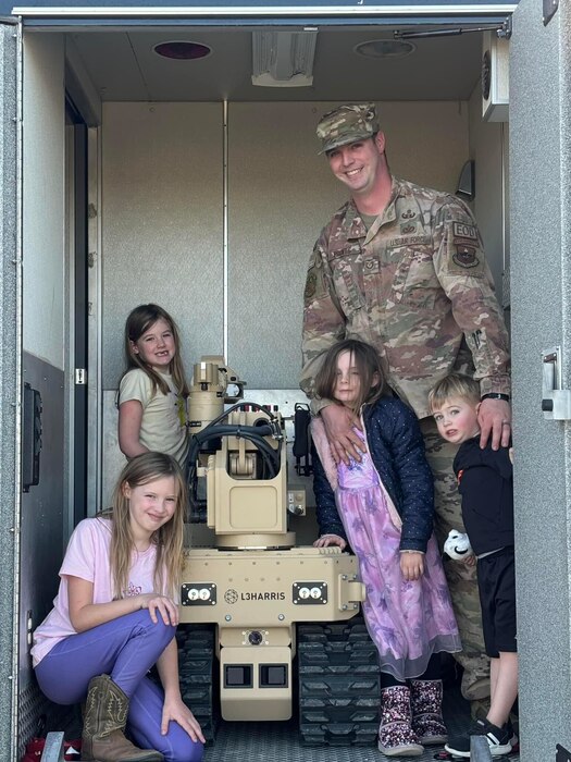 An Airman stands next to an EOD robot with children.