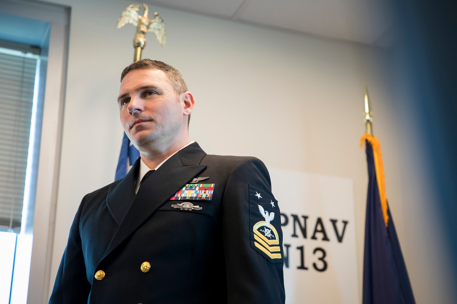 Navy Master Chief Petty Officer wears service dress blues in the Navy's N13 office, highlighting the Robotics Warfare Specialist rating badge