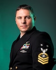 Navy Master Chief Petty Officer poses for a photo in service dress blues, highlighting the Robotics Warfare Specialist rating badge