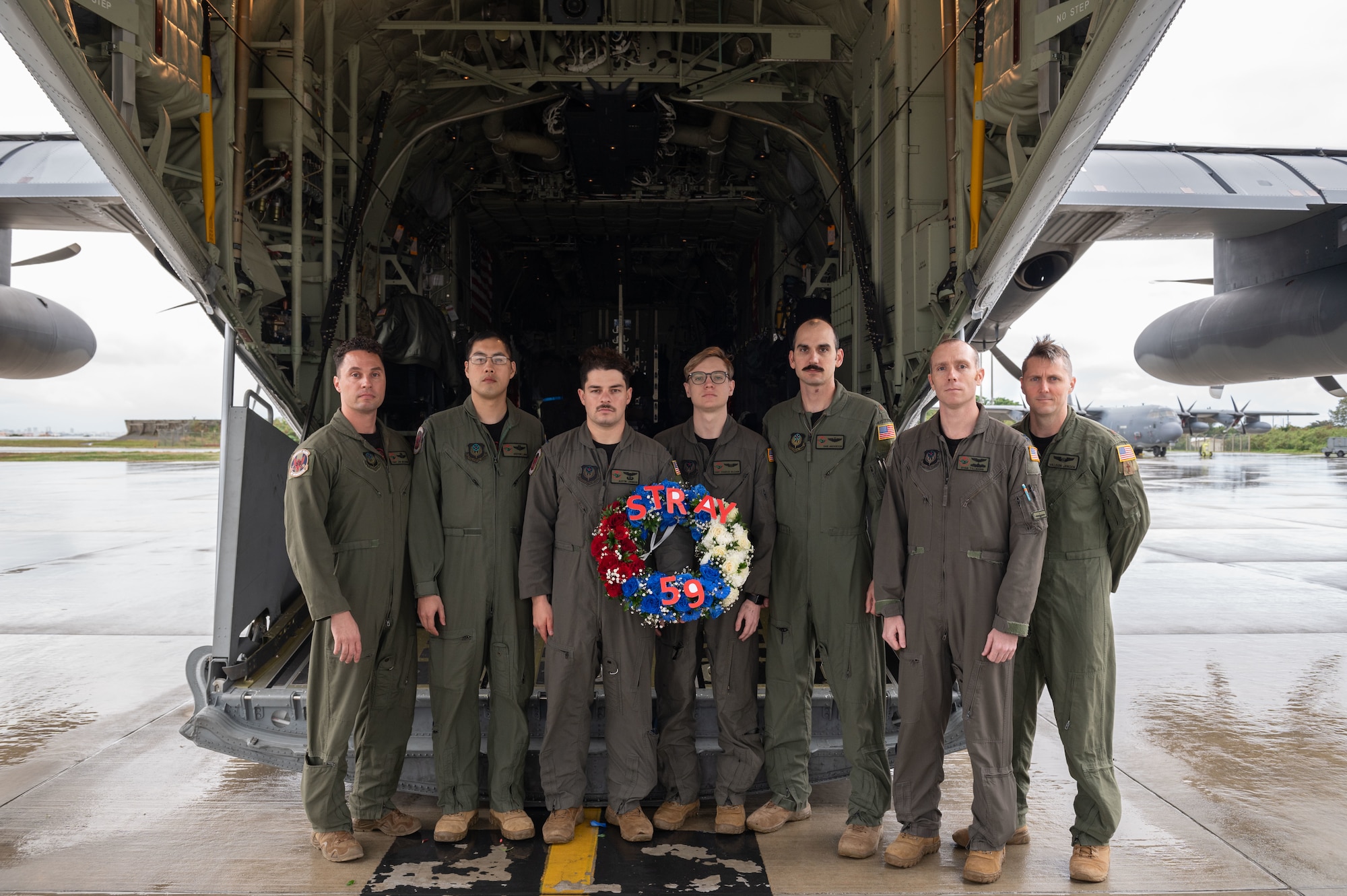 Airmen stand in front of an MC-130J with a STRAY 59 memorial wreath