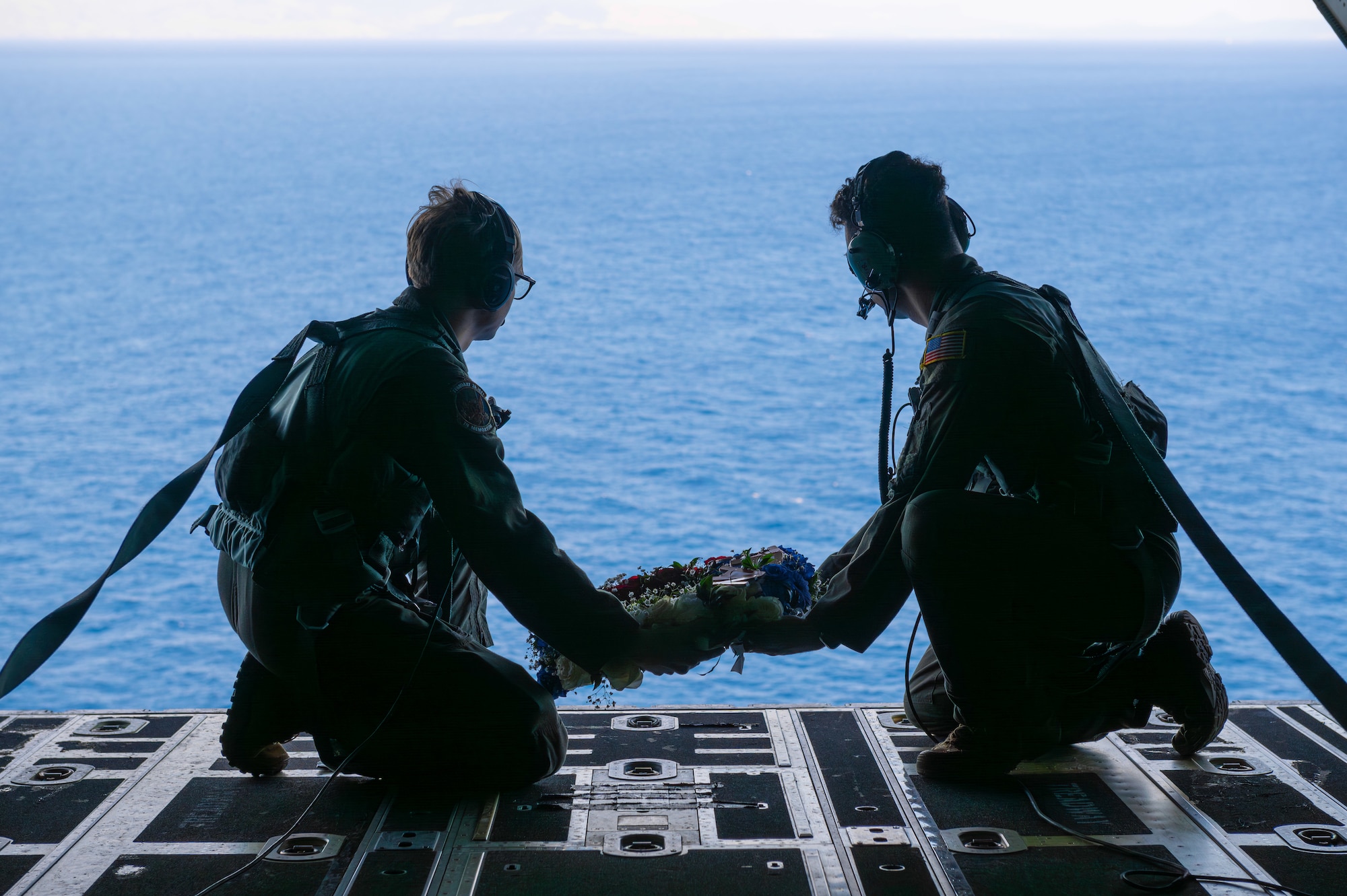 Airmen hold a memorial wreath over the coast of the Philippines in the back of an open MC-130J Commando II