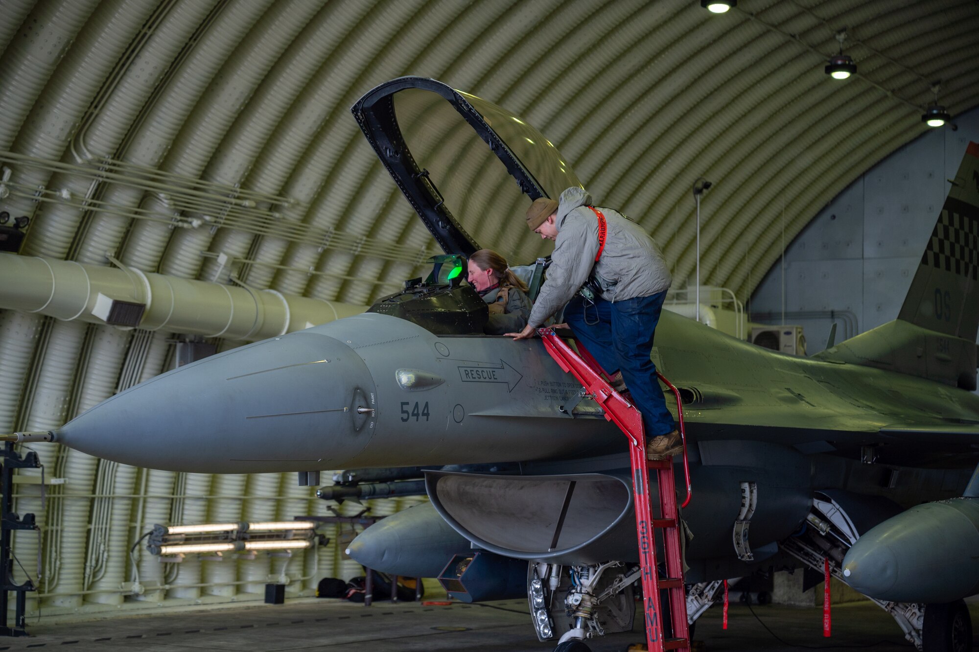 A crew chief helps a pilot into a cockpit.