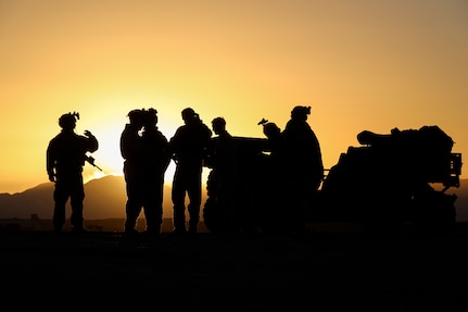 A group of Marines are shown in silhouette standing near a tactical vehicle.