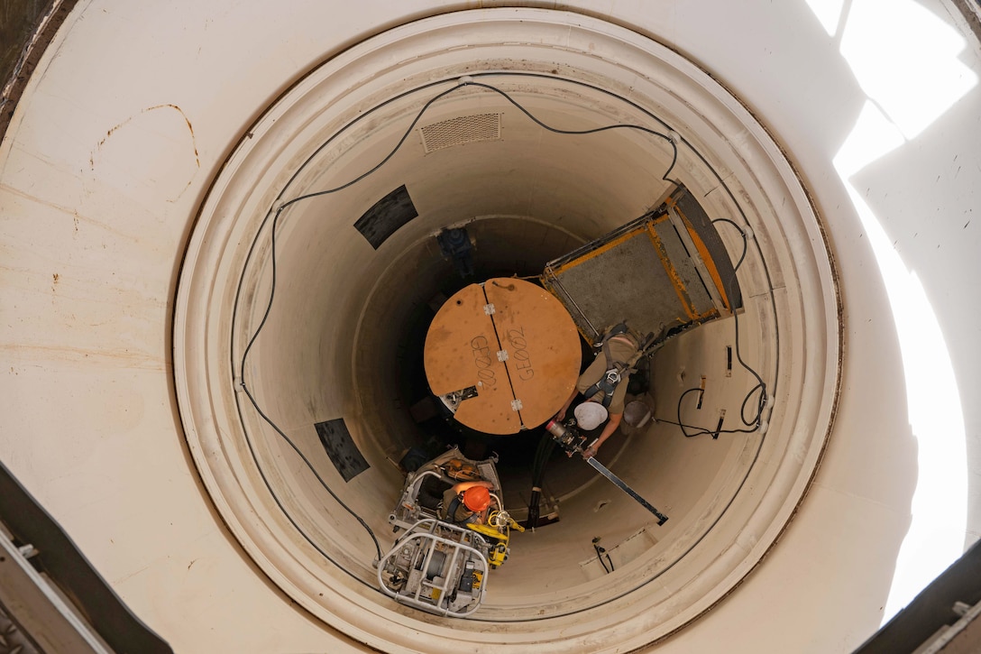 Two airmen stand on platforms as they perform work inside the cone of a missile in a photo taken from above.