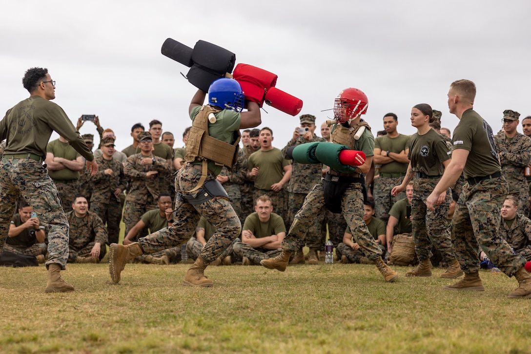 A group of Marines watch as two Marines in protective gear participate in a pugil stick match.