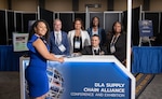 Six people pose for photo at a blue and white booth. Woman in front wearing blue dress.