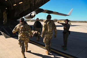 Capt. Teodoro Olivares, left, a 433rd Aeromedical Evacuation Squadron flight nurse, and Staff Sgt. Rheannon Pionek, right, a 433rd AES technician, direct Texas State Guardsmen as they load a simulated patient during joint medical training at Joint Base San Antonio-Lackland, Texas on Feb. 24, 2024.