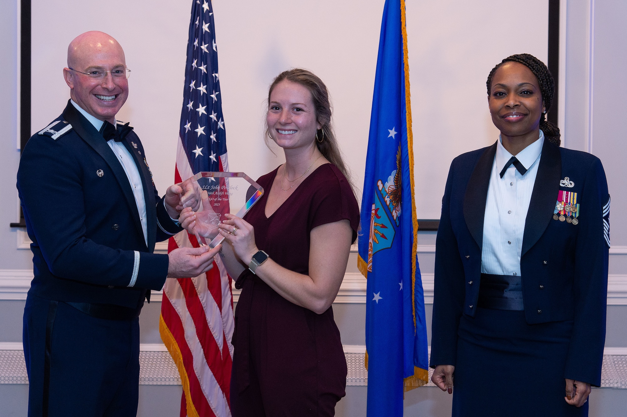 U.S. Air Force Col. Chris McDonald, left, 436th Airlift Wing commander, and U.S. Air Force Chief Master Sgt. Carolyn Russell, right, 436th AW command chief, present Tessa Portlock, center, with a trophy during the 2023 436th AW Annual Awards Ceremony held at the Hartly Volunteer Fire Company in Hartly, Delaware, Feb. 23, 2024. She accepted the trophy on behalf of her husband U.S. Air Force 1st Lt. John Portlock, 436th Operations Group annual award winner, who was recognized as the wing’s Company Grade Officer of the Year. (U.S. Air Force photo by Roland Balik)