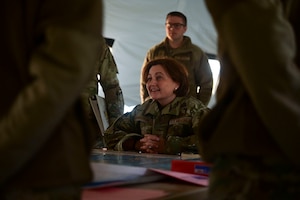 Inside a tent, a female Air Force leader is listening to an intelligence briefing from student military members.
