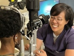 Smiling optometrist using equipment to check a patient's eyes.