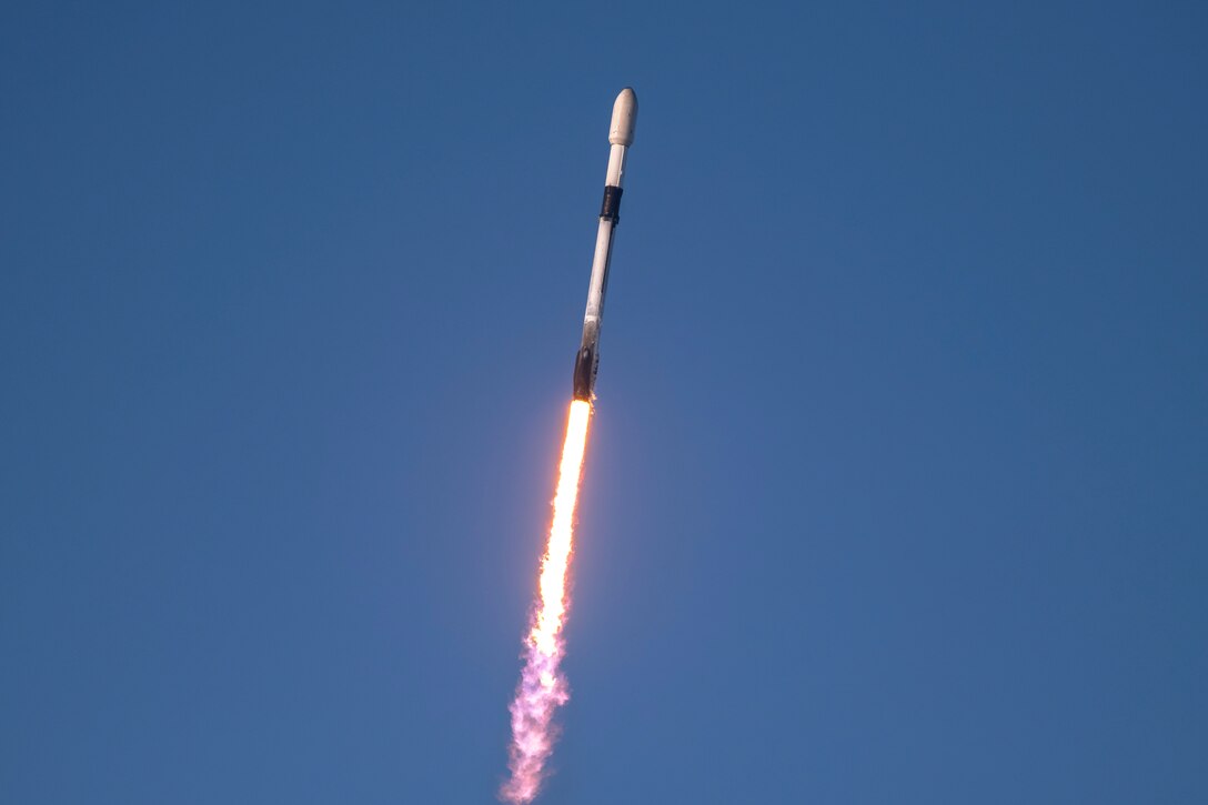 A streak of fire follows a rocket as it launches into a blue sky.