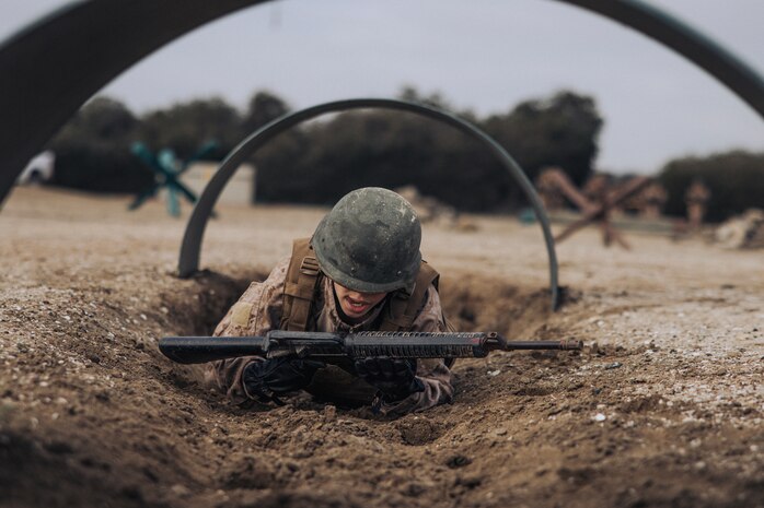 A U.S. Marine Corps recruit with Mike Company, 3rd Recruit Training Battalion low crawls under an obstacle on the bayonet assault course at Marine Corps Recruit Depot San Diego, California, Feb. 27, 2024. Recruits conduct the bayonet assault course and pugil stick events to practice skills in hand-to-hand combat and push the limits of their physical endurance. (U.S. Marine Corps photo by Cpl. Alexander O. Devereux)