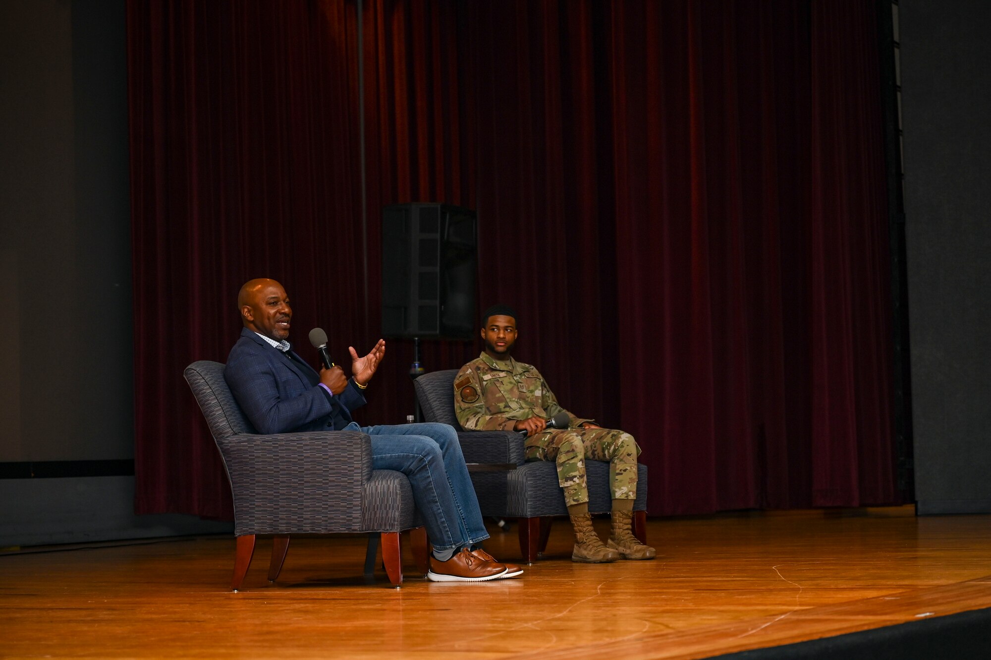 Men sit in chairs on a stage.