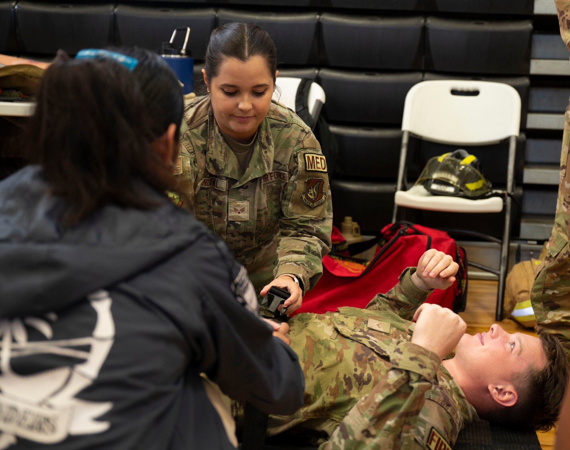 U.S. Air Force Senior Airman Sierra Sandoval, 36th Health Care Operations Squadron emergency medical technician and Airman 1st Class David Miller, 36th Civil Engineer Squadron firefighter, demonstrate strapping a patient on to a stretcher during the Tiyan High School Health Fair in Barrigada, Guam, Feb. 23, 2024. At the fair Airmen from the 36th CES and 36th Medical Group demonstrated carrying a patient, applying a tourniquet, and walked students through various physical therapy exercises. (U.S. Air Force photo by Airman 1st Class Spencer Perkins)