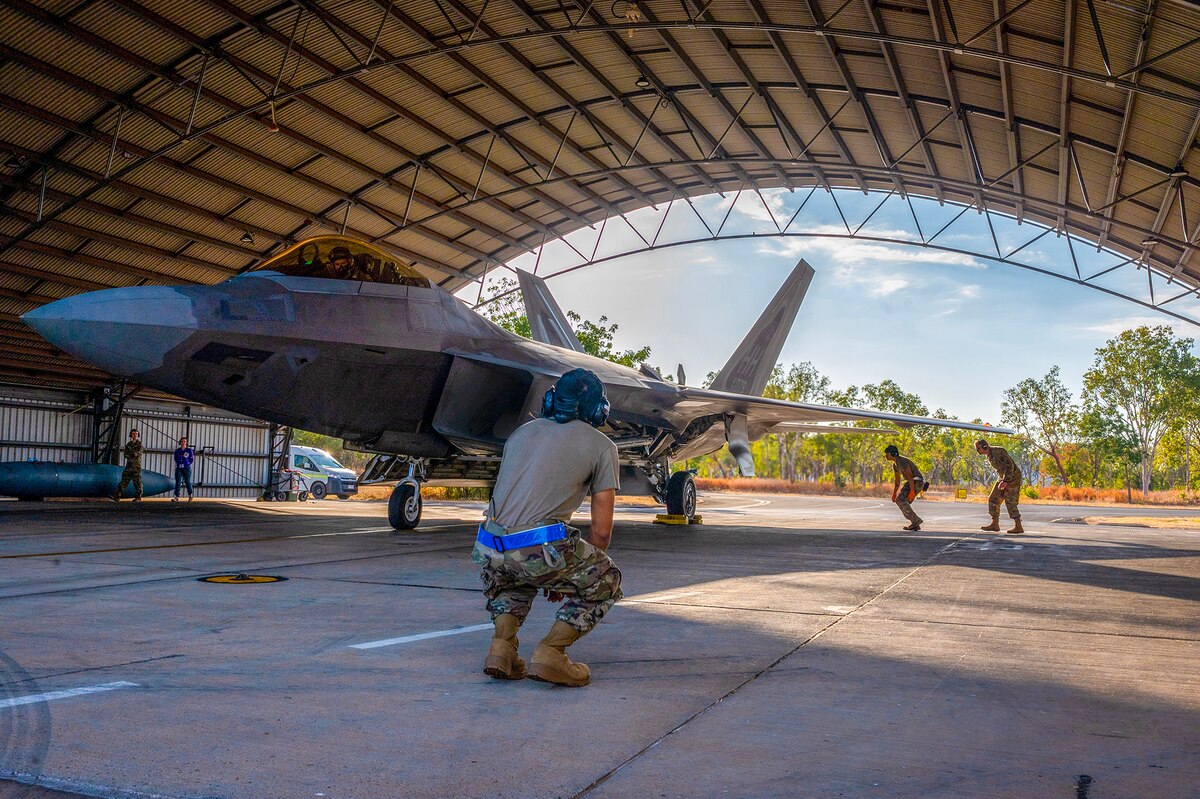 Service members in uniform inspect a jet.