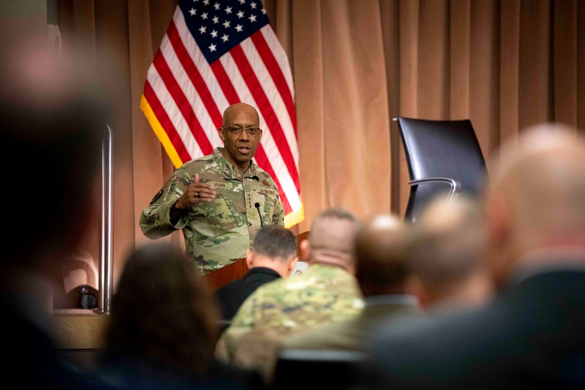 A man speaks to an audience while sitting on a stage.