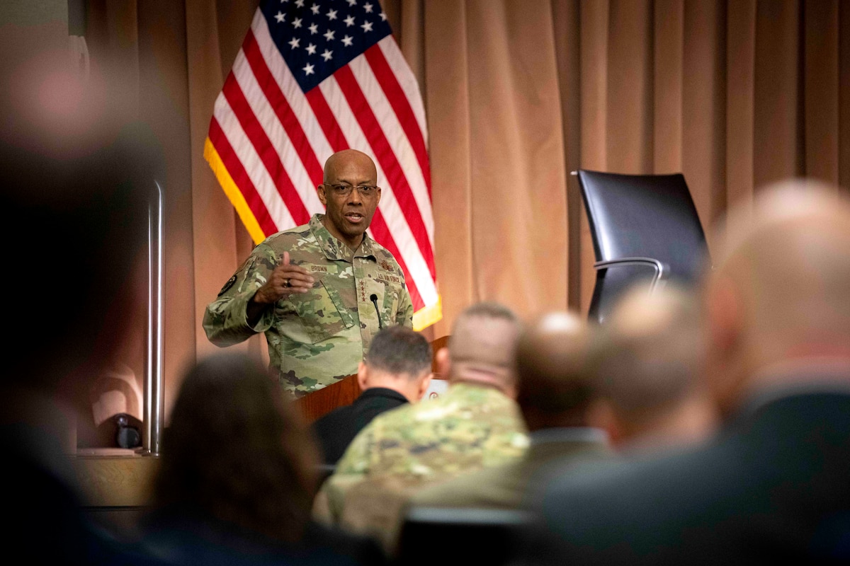 A man speaks to an audience while sitting on a stage.