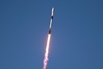 A streak of fire follows a rocket as it launches into a blue sky.