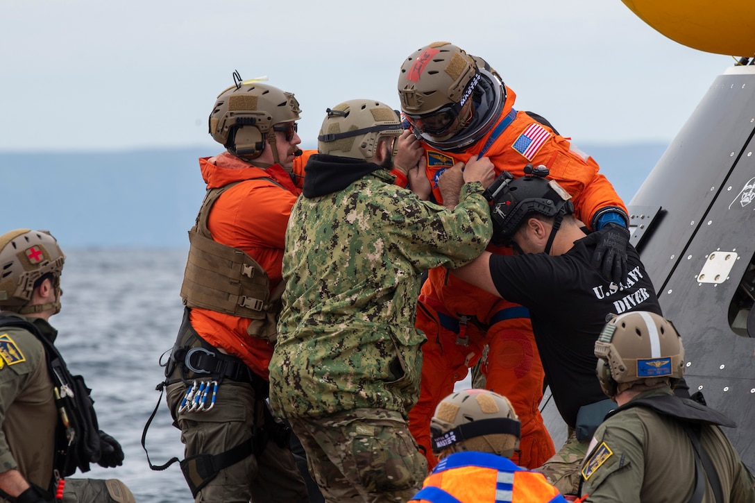 A group of sailors assist an astronaut from a capsule in open water.