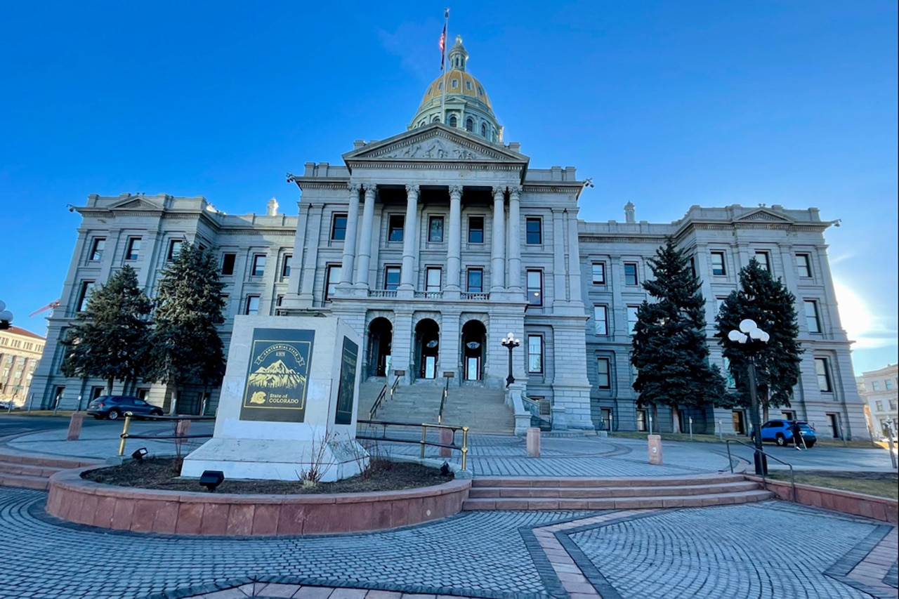 A white granite building with a gold dome is in a stone courtyard.