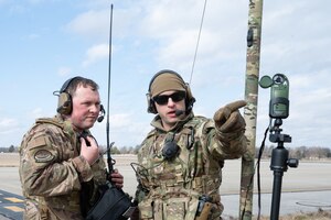 MSgt. Rodney points to a wind sensor while speaking to TSgt. Marple, who prepares to relay the information over radio to a pilot.