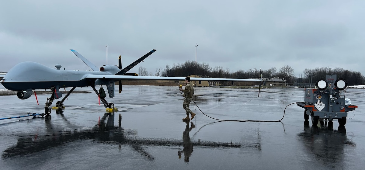 An aircraft maintainer at the 174th Attack Wing at Hancock Field Air National Guard Base, Syracuse, New York, connects the power cable from the 400 Hz Aircraft Power Lightcart, or 400 APL prototype to an MQ-9, or Reaper, to test its ability to power the aircraft through a series of technical orders on the flightline.