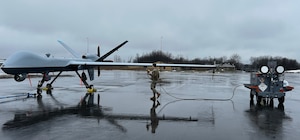 An aircraft maintainer at the 174th Attack Wing at Hancock Field Air National Guard Base, Syracuse, New York, connects the power cable from the 400 Hz Aircraft Power Lightcart, or 400 APL prototype to an MQ-9, or Predator to test its ability to power the aircraft through a series of technical orders on the flightline.