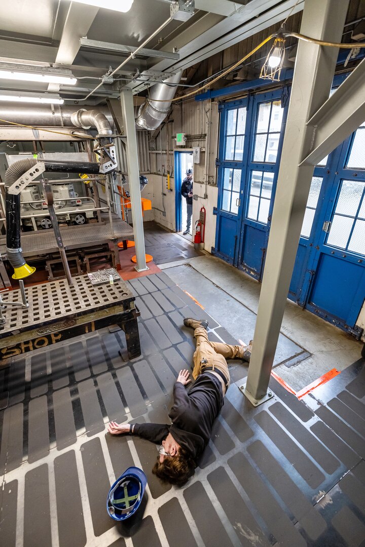 Dave Hofmeister, supervisor, Shop 75, IRR Ship Dismantling, at Puget Sound Naval Shipyard & Intermediate Maintenance Facility in Bremerton, Washington, lays on the floor Feb. 12, 2024, during a "1001 Steps Supervisor/Work Leader Safety Course" confined-space simulation, as Andrew Gorton, supervisor Shop 06, Logistics, monitors the situation from outside the simulated dangerous environment. (U.S. Navy photo by Jeb Fach)