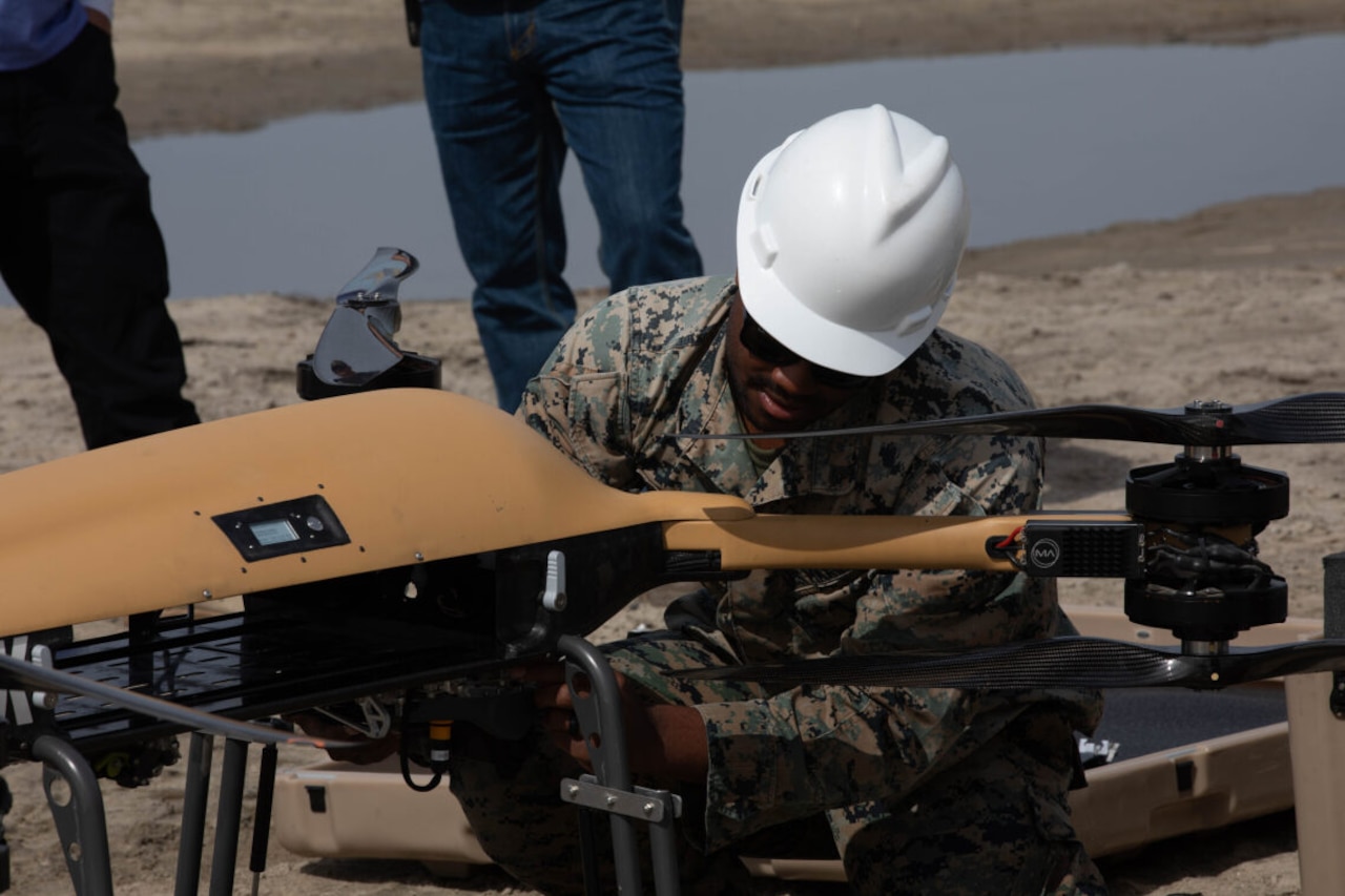 A service member wearing a hard hat handles an unmanned aerial vehicle.