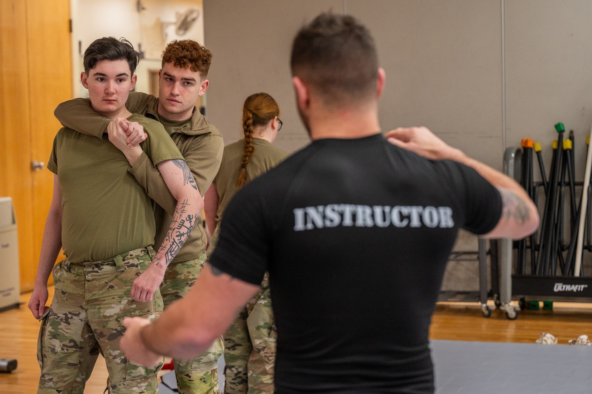 U.S. Air Force Senior Airman Jordan Smith, 621st Air Control Squadron weapons director, left, and Airman 1st Class Colin Rumping, 621st ACS weapons director, receive instructions on a combatives move from Staff Sgt. Kyle Virgillio, 5th Combat Communications Support Squadron master combatives instructor during a combatives instructor certification course at Osan Air Base, Republic of Korea, Feb. 23, 2024. Having the ability to become certified in combatives gives Airmen from the 51st Fighter Wing a more accessible way to become certified and grow as multi-capable Airmen. The 621st ACS impacts the “Fight Tonight” mission by supporting training and contingency operations of the 51st FW, providing lethal tactical battle management for the Air Component Commander during armistice and war. (U.S. Air Force photo by Airman 1st Class Chase Verzaal)