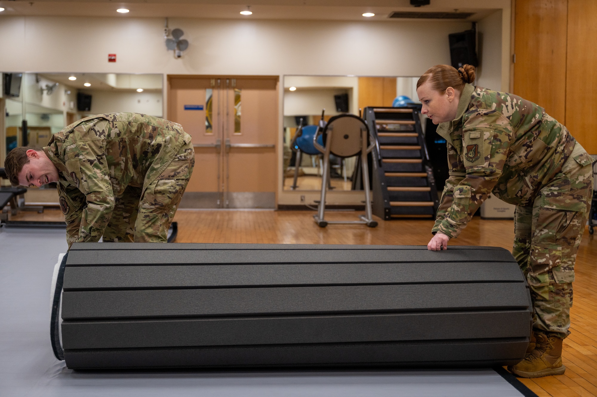 U.S. Air Force 1st Lt. Demetre Fontaine, 621st Air Control Squadron air battle manager, left, and Staff Sgt. Adrian Reardon, 607th Air Operations Center comptroller, unroll a mat before a combatives instructor certification course at Osan Air Base, Republic of Korea, Feb. 23, 2024. Certifying Airmen as combatives instructors enhances operational efficiency by enabling the widespread dissemination of essential combat readiness skills throughout the installation. The 621st ACS and 607th AOC intend to utilize the new certifications to tailor a combatives program to their operational needs and enhance their ability to support the 51st Fighter Wing during training and contingencies. (U.S. Air Force photo by Airman 1st Class Chase Verzaal)