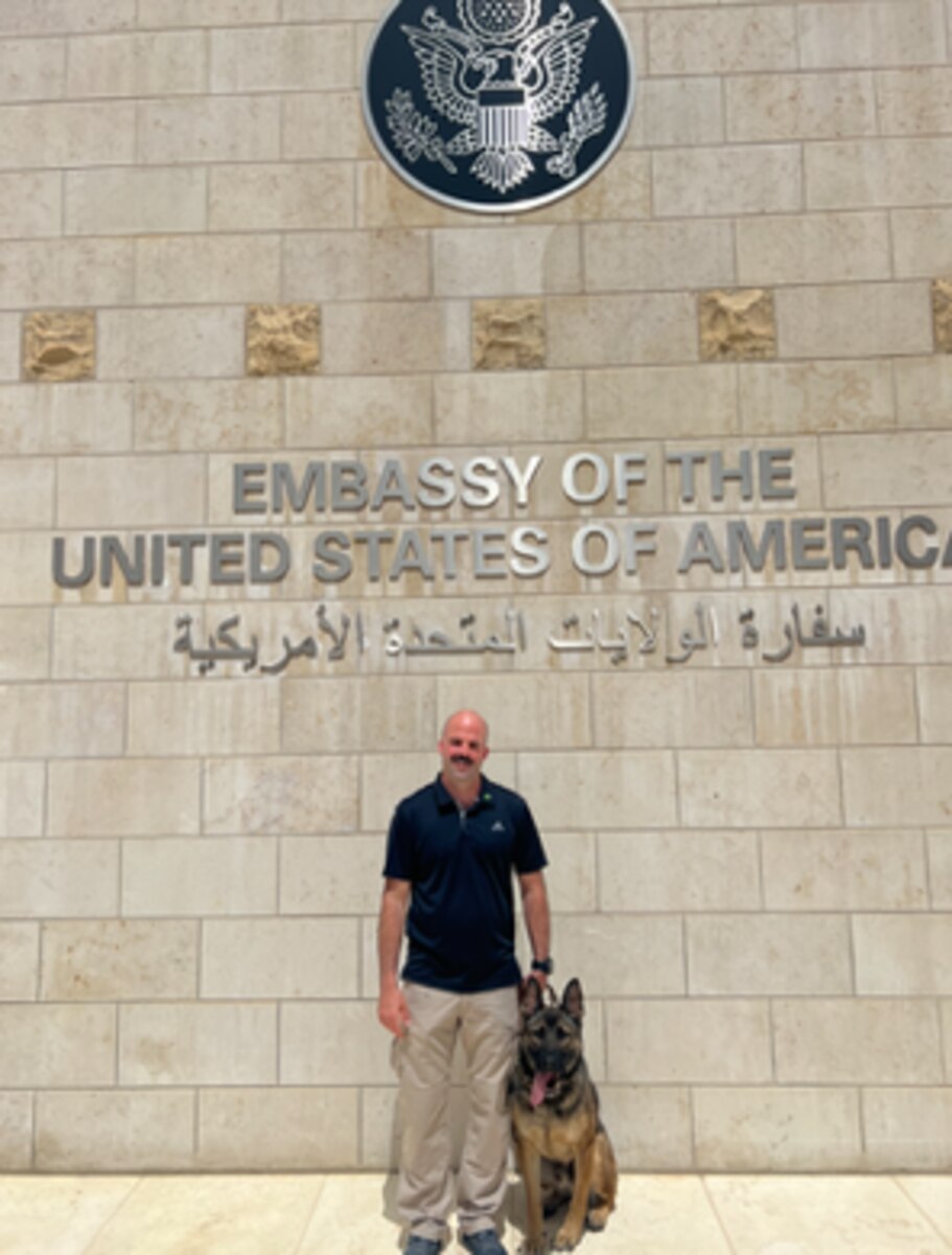 handler and his dog in front of an embassy building
